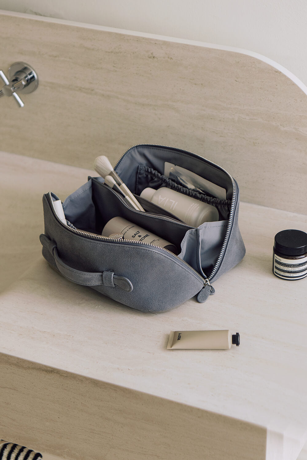 Large capacity blue travel makeup bag open on bathroom counter, showing wide opening for easy access