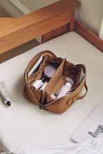 Lifestyle shot of caramel handheld cosmetic bag on window sill, aesthetic travel organizer