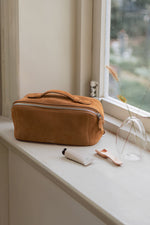 Large capacity caramel brown makeup bag open on bed, showing spacious interior for travel essentials
