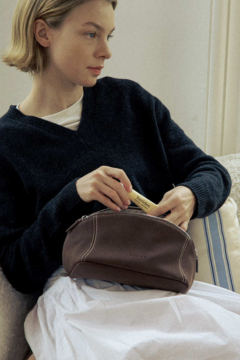 Woman holding a black leather makeup bag for travel, stylish handheld cosmetic bag.