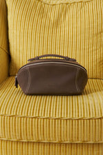 Black leather makeup bag sitting on yellow sofa, premium travel toiletry bag organizer.
