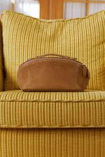 Camel brown makeup bag resting on yellow sofa, retro style travel cosmetic bag.