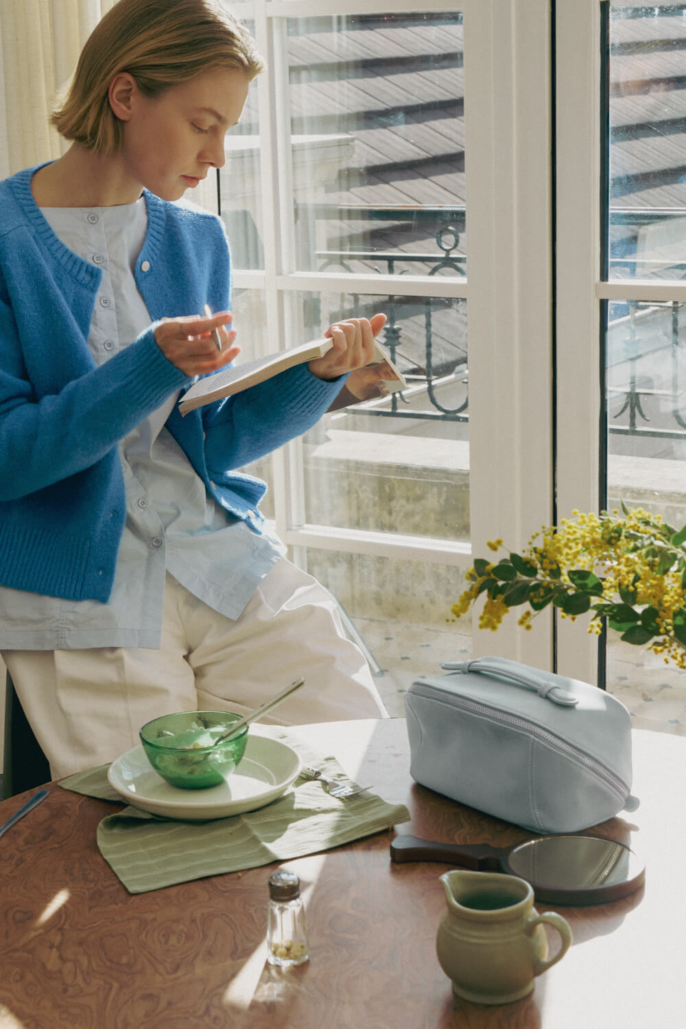 Light blue makeup bag lifestyle shot by window, daily use travel cosmetic bag.
