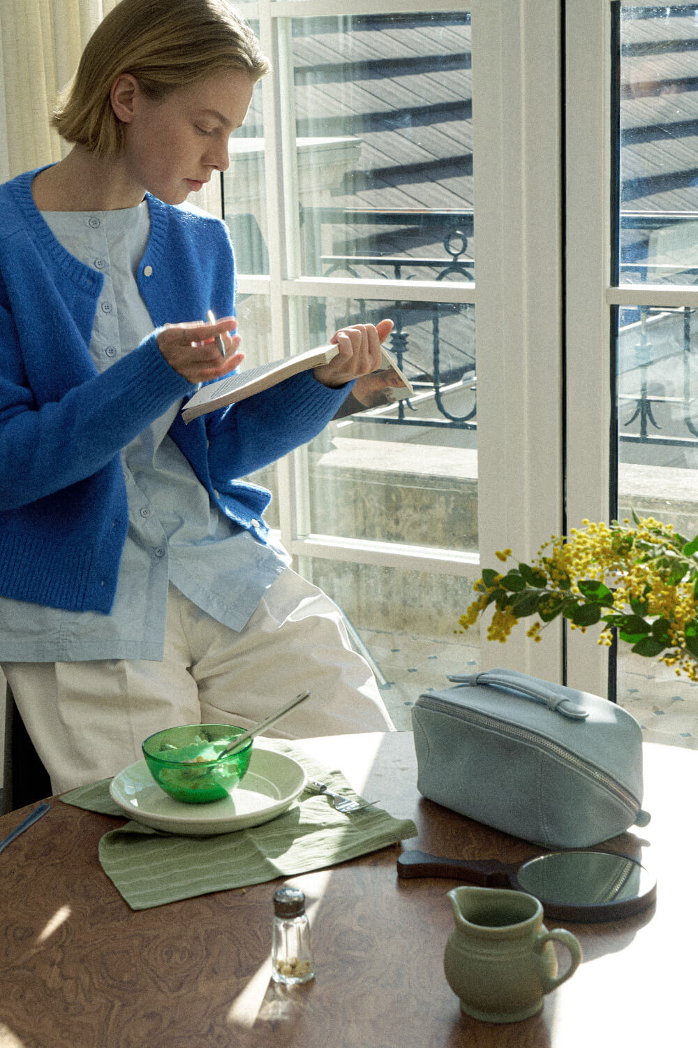 Light blue makeup bag lifestyle shot by window, daily use travel cosmetic bag.