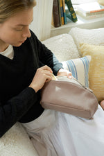 Woman looking into mauve makeup bag, practical travel toiletry bag usage.